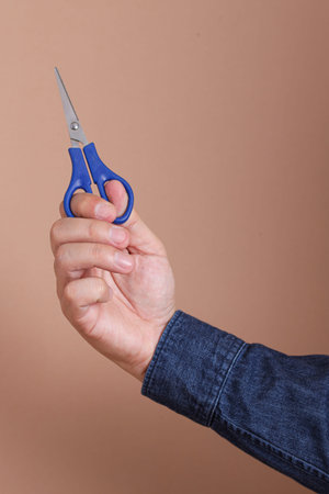 Close up of asian man hand holding scissors isolated on brown background
