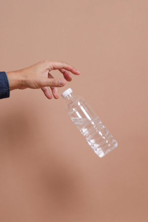 Asian man's hand holds bottle of water or transparent plastic bottle, isolated on  blue background....