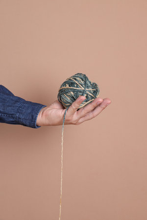 Asian manâs hand holding a ball of wool yarn isolated on brown background, studio shot. hobby.  Crochet and knitting. Working space.の写真素材