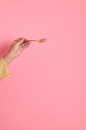 Happy Chinese new year. Asian Chinese energetic senior man wearing red traditional cheongsam qipao or changshan dress with gesture of hand holding golden fork isolated on pink background.の写真素材