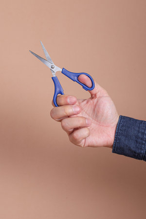 Close up of asian man hand holding scissors isolated on brown backgroundの写真素材