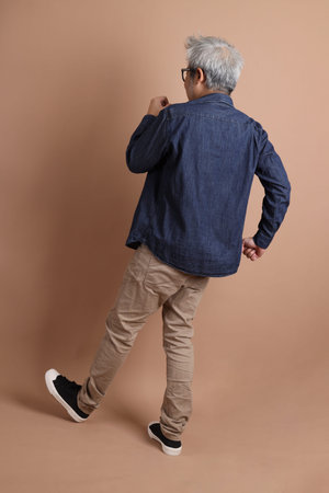 Asian energetic senior man with glasses posing  isolated on the brown background with casual...