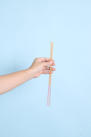 HAPPY SONGKRAN DAY. Asian tourist senior man in summer clothing and sunglasses with gesture of hand holding the incense sticks  isolated on blue background. Songkran festival. Thai New Year's Day.の写真素材
