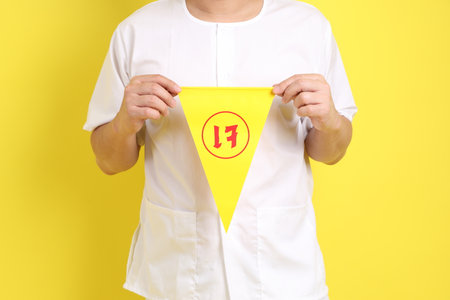 Senior man in white color with gesture of holding Chinese vegetarian festival flag isolated on yellow background. J festival,  Translation for Chinese and Thai text is refrain eating meat or symbol of vegetarian festival.の写真素材