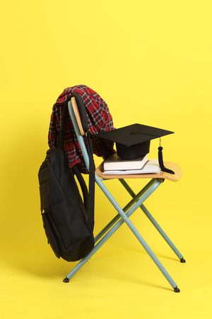 Back to school concept with school books, textbooks, backpack and stationery supplies on classroom chair isolated on yellow background. Studying abroad, Gen Z, E-learning.の写真素材