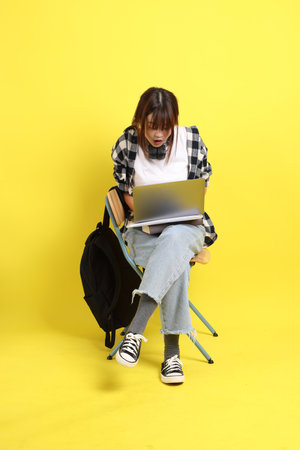 Asian college female student wearing plaid shirt carry school bag and book, gesture of sitting and Holding laptop. Studying abroad, Gen Z, E-learning.の写真素材