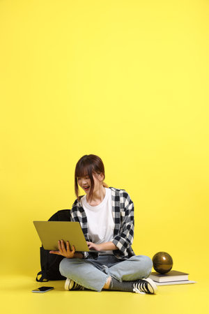 Asian college female student wearing plaid shirt carry school bag and book, gesture of sitting and working on laptop. Studying abroad, Gen Z, E-learning.の写真素材