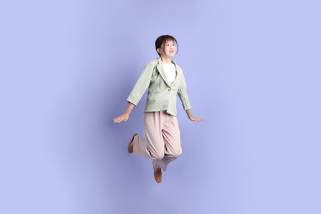 A young asian Businesswoman in formal outfit with gesture of jumping isolated on purple background....