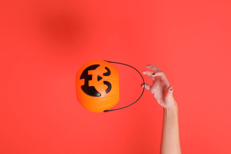 HAPPY HALLOWEEN DAY, female hand with black nails holding Jack-o-Lantern Pumpkin isolated on orange background.の写真素材
