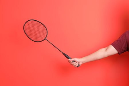 Asian man hand holds Badminton racket on orange background. Exercise and sport concept.
