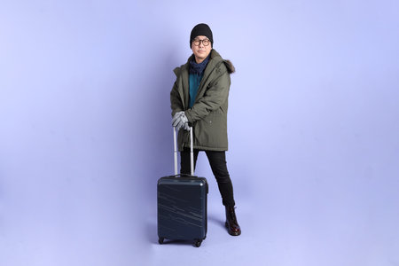 The Asian senior man wears winter clothes with gesture of  holding suitcase isolated on purple background.の写真素材