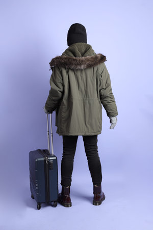 The Asian senior man wears winter clothes with gesture of  holding suitcase isolated on purple...