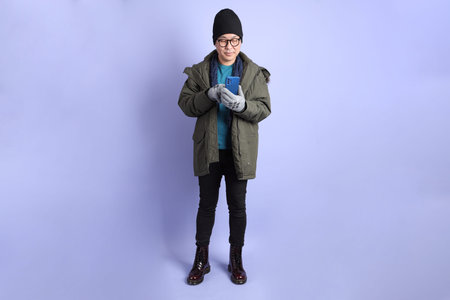 The Asian senior man wears winter clothes with gesture of  Holding mobile phone isolated on purple background.の写真素材