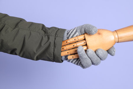 Hand of mannequin shake hands with human hand on isolated blue background. Symbol, teamwork.の写真素材