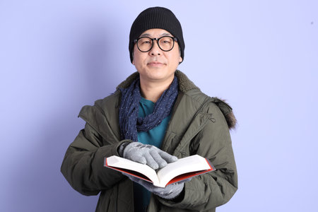 The Asian senior man wears winter clothes with gesture of  holding a book isolated on purple...