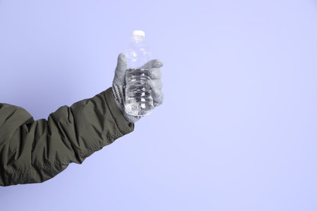 The Asian senior man wears winter clothes with gesture of   holding water bottle isolated on purple background.の写真素材