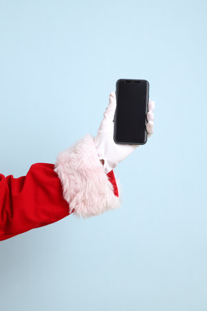 Merry Christmas, Cheerful senior man celebrate winter holidays is holding mobile phone, wearing Santa Claus costume isolated on yellow and blue background. Merry Xmasの写真素材