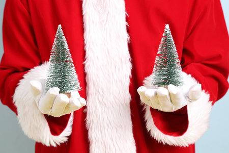 Merry Christmas, Cheerful senior man celebrate winter holidays is holding little decorative Christmas tree, wearing Santa Claus costume isolated on blue background. Merry Xmasの写真素材
