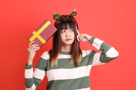 Asian woman wearing Christmas or winter clothes with Santa cap, holding a pile of presents in her...