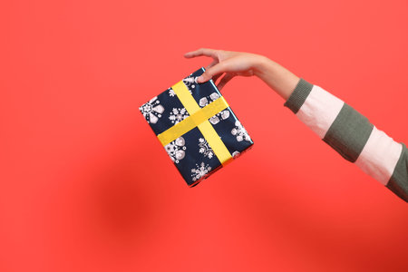A close-up of a hand wearing a green stripe pattern sweater holding up a gift or present box,...