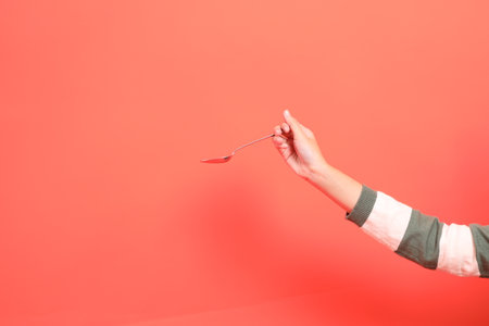 A close-up of a hand wearing a green stripe pattern sweater holding spoon or fork a gift or present box, isolated against a red background. Merry Christmas.の写真素材