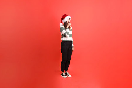 Asian woman wearing Christmas or winter clothes with Santa cap with gesture of smelling, cover nose isolated on red background. Xmas, Santa Claus.の写真素材