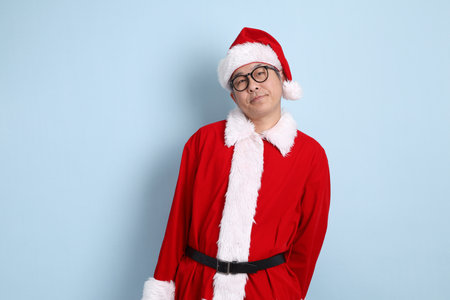 Asian Santa Claus in eyeglasses in Santa cap with gesture of Serious, arm crossed isolated on blue background, Xmas.の写真素材