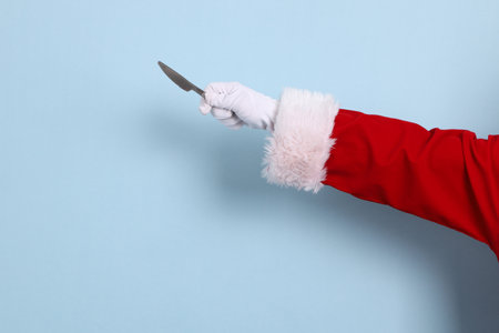 A close-up of a hand of Santa Claus holding up knife, isolated against a blue background. Merry Christmas.の写真素材