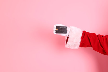 Merry Christmas, Cheerful senior man celebrate winter holidays is holding black credit card, wearing Santa Claus costume isolated on pink background. Merry Xmasの写真素材