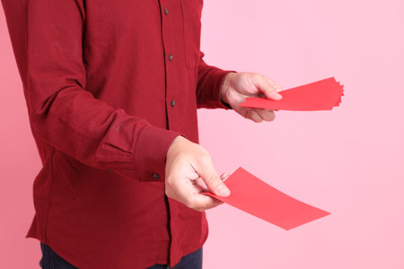 Happy Chinese New Year, asian senior man in formal and casual red shirts with gesture of hand  holding Chinese Red envelopes isolated on the pink background.の写真素材