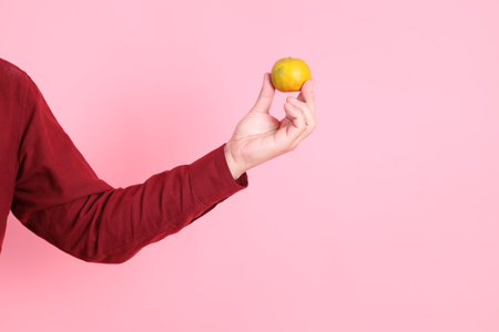 Happy Chinese New Year, asian senior man in formal and casual red shirts with gesture of  hand holding Tangerine or Orange isolated on the pink background.の写真素材