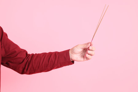 Happy Chinese New Year, asian senior man in formal and casual red shirts with gesture of hand holding the incense sticks isolated on the pink background.の写真素材