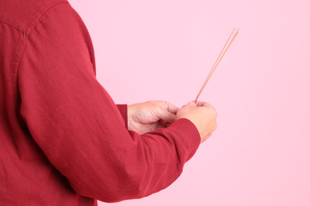 Happy Chinese New Year, asian senior man in formal and casual red shirts with gesture of hand holding the incense sticks isolated on the pink background.の写真素材