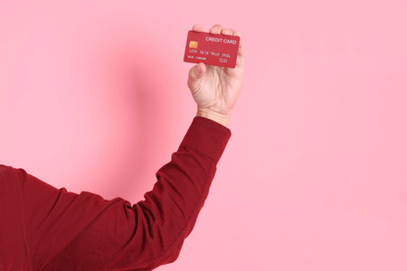 Happy Chinese New Year, asian senior man in formal and casual red shirts with gesture of hand Holding red credit card isolated on the pink background.の写真素材