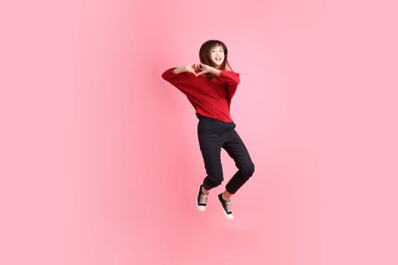 Happy Chinese New Year, young  female asian woman in red casual t-shirt with gesture of Jumping isolated on the pink background. Gen Zの写真素材