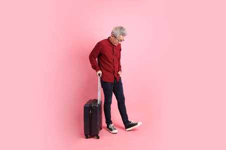 Happy Chinese New Year, asian senior man in formal and casual red shirts with gesture of holding suitcase isolated on pink background.の写真素材