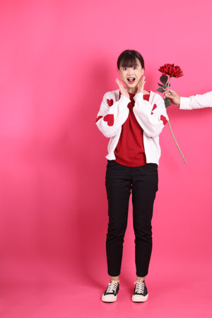 St Valentine's Day, Asian woman in red t-shirt or casual clothes, red heart-shaped shaped shirt jacket  with gesture of  Holding flower isolated on pink background. Gen Zの写真素材