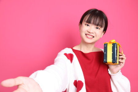 St Valentine's Day, Asian woman in red t-shirt or casual clothes, red heart-shaped shirt jacket with gesture of holding gift box isolated on pink background. Gen Zの写真素材