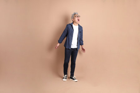 Asian senior man in casual clothes with gesture of shouting, isolated on brown background.の写真素材