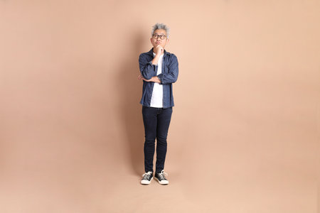Asian senior man in casual clothes with gesture of thinking isolated on brown background.の写真素材