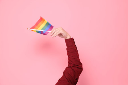 Asian senior man in formal and casual red shirts with gesture of Holding Rainbow Pride Flags in both hands isolated on pink background.の写真素材