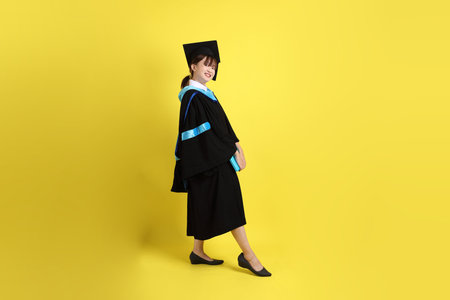 Female university student in blue graduation gowns and caps and holding diplomas with gesture of...
