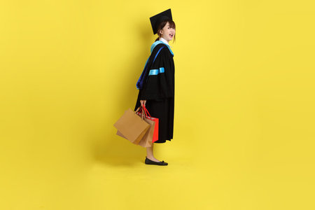 Female university student in blue graduation gowns and caps with gesture of holding shopping bag...