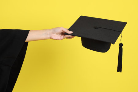 University student in blue graduation gowns gesture of holding graduation caps isolated on yellow background. Gen Z, fresh graduate, education, first jobberの写真素材