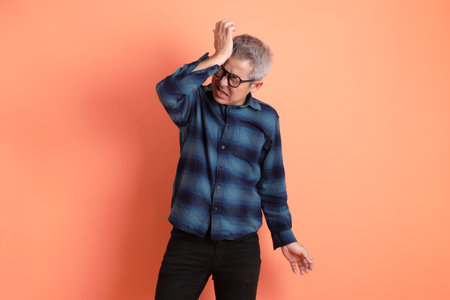 Senior man in plaid casual clothes wearing glasses with gesture of stress isolated on orange background.の写真素材