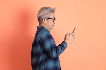 Asian senior man in plaid casual clothes wearing glasses with gesture of holding mobile phone...