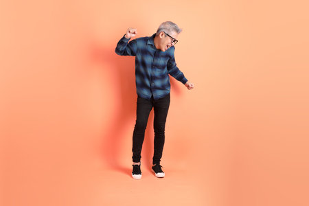 Asian senior man in plaid casual clothes wearing glasses with gesture of dancing isolated on orange background.の写真素材