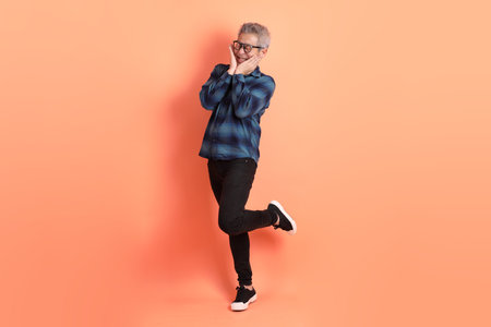 Asian senior man in Green plaid casual clothes wearing glasses with gesture of Standing and smiling isolated on orange background.の写真素材
