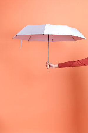 Short hair asian woman in red casual long sleeve t-shirt with gesture of hand Holding blue and pink Umbrella isolated on orange background.の写真素材