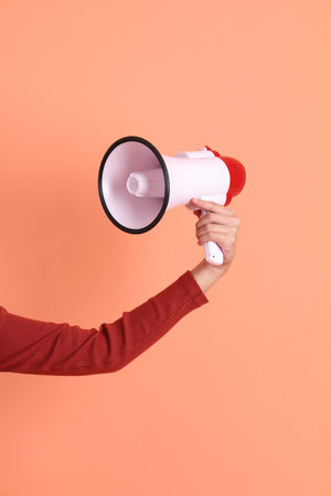 Short hair asian woman in red casual long sleeve t-shirt with gesture of shouting, holding megaphone isolated on orange background.の写真素材
